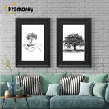 Two antique black picture frames with black mounts displaying black and white artwork hanging above a couch against a brick wall