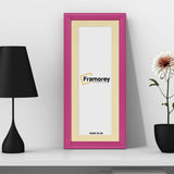 Antique Style Panoramic Size Pink Photo Frame with black mount leaning with the wall on the floor and a black lamp and a flower pot placed near it.