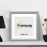 Antique Style Square Size Silver Photo Frame with white mount on a white surface with a lamp and a flower with pot on its sides.