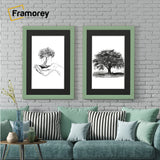 Two antique style green picture frames with black mounts displaying black and white artwork hanging above a couch against a brick wall