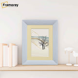Limed White Poster Frame With Ivory Mount photo frame on a wooden bench standing with the wall.