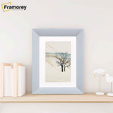 Limed White Poster Frame With White Mount on a wooden shelf standing with the wall.