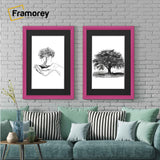 Two antique style pink picture frames with black mounts displaying black and white artwork hanging above a couch against a brick wall