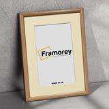 Side view of a thin Oak Photo Frame With Ivory Mount leaning with a wall on a floor.