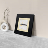 Side view of a Square Black Photo Print Frame With Ivory Mount is leaning with the wall on a wooden table.
