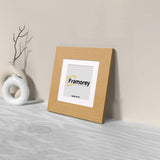 Side view of a Square Oak Photo Print Frame with White Mount is leaning with the wall n a wooden surface.