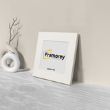 Square White Photo Frame Side View is leaning with the wall on a wooden surface.