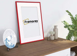 Side view of a Thin Red Photo Frame With White Mount on a wooden piece standing with the wall and a plate placed on its left.