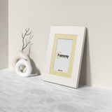 Side view of a White Picture Frame with Ivory mount Poster Frame with a Framorey loo in the frame and the frame is standing with the wall on a wooden table.