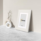 Side view of a White Photo Frame with White mount Poster Frame is leaning with the all on a wooden surface.