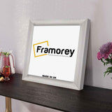 Side view of a White Reverse Square Style Poster Frame leaning on the wall on a wooden table.