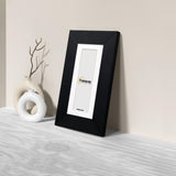 Side view oof a Panoramic Black Photo Print Frame with White Mount is Leaning with the wall on a wooden surface.