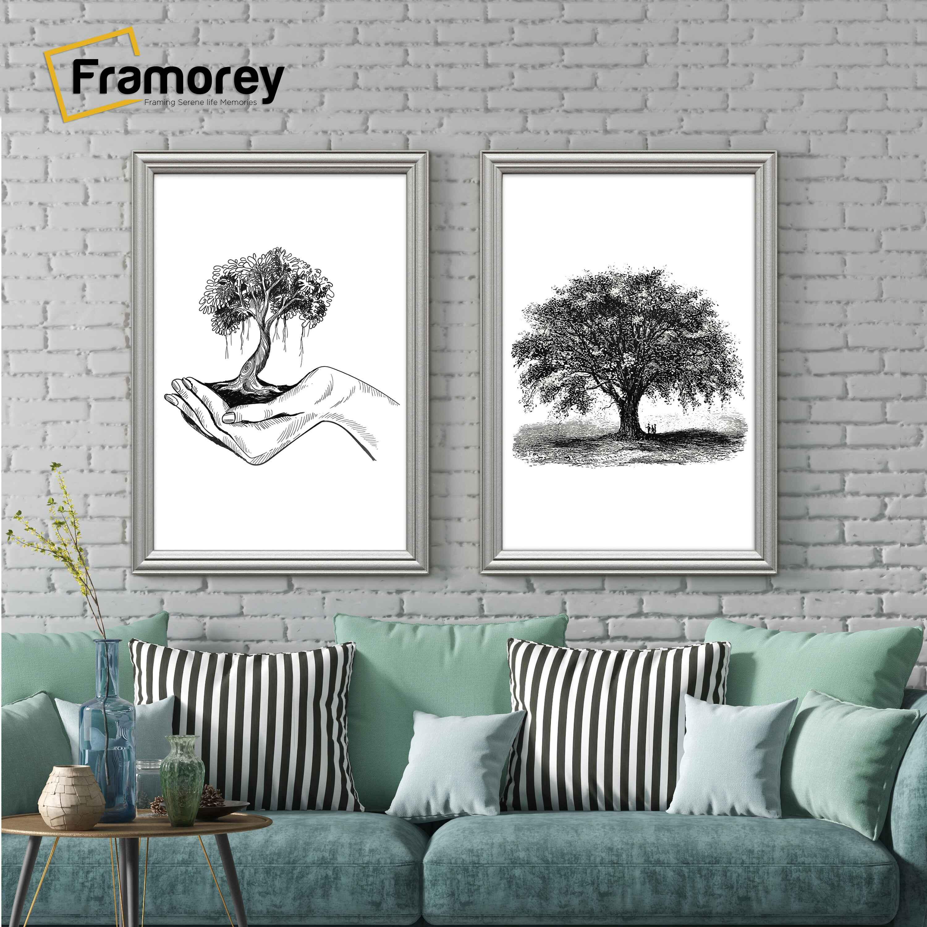 Two antique style silver picture frames displaying black and white artwork hanging above a couch against a brick wall