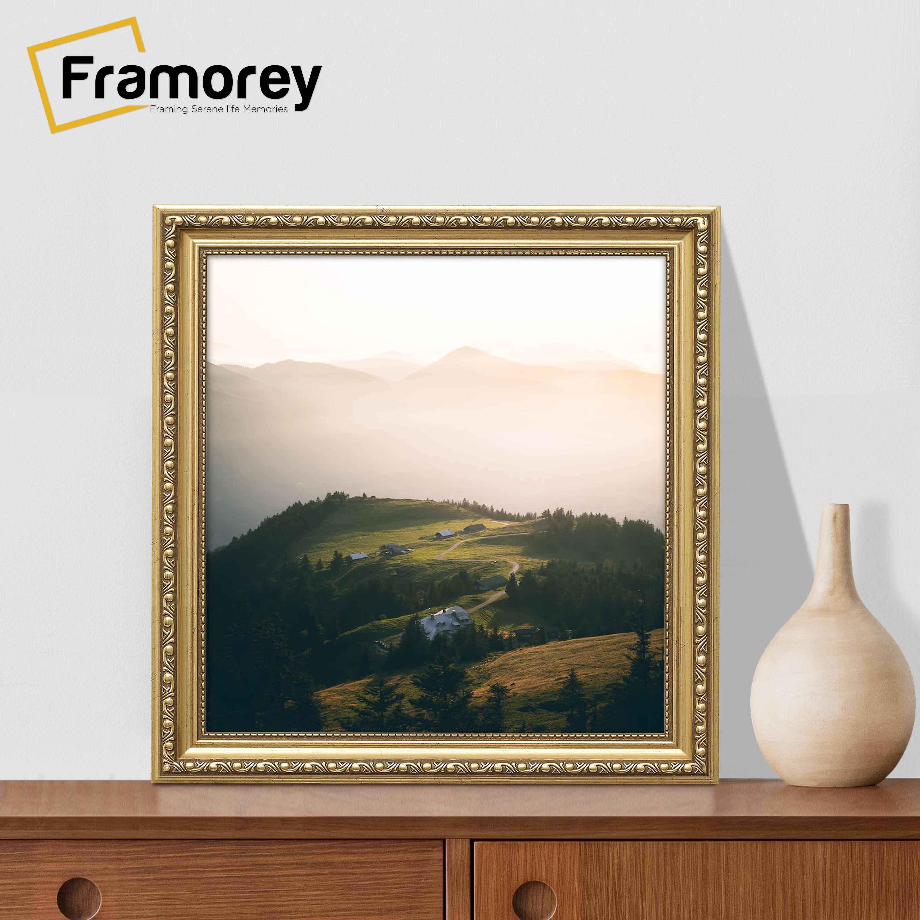 Square gold shabby photo frame on a table with a vase near it.