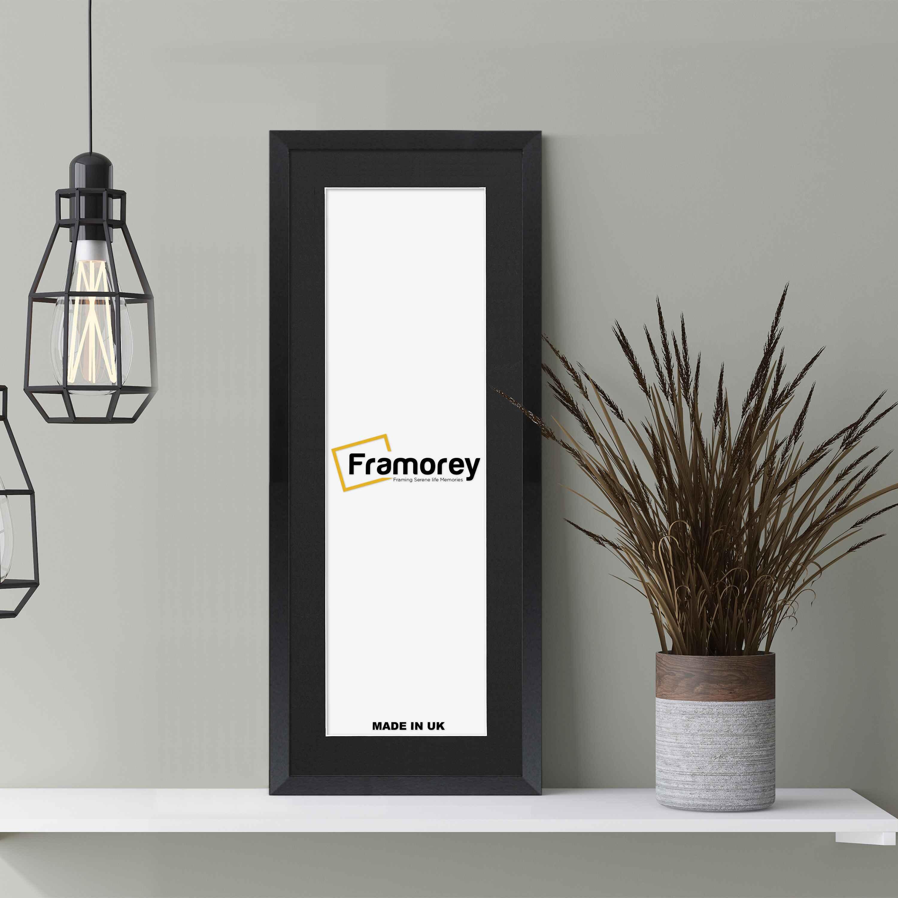 Thin Matt Panoramic Black Photo Frame With Black Mount on a wooden table leaning with the wall and two lamps just hanging on its left.