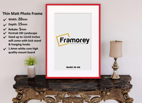 Thin Red Photo Frame With White Mount on a wooden table standing with the wall and some detail on its left.