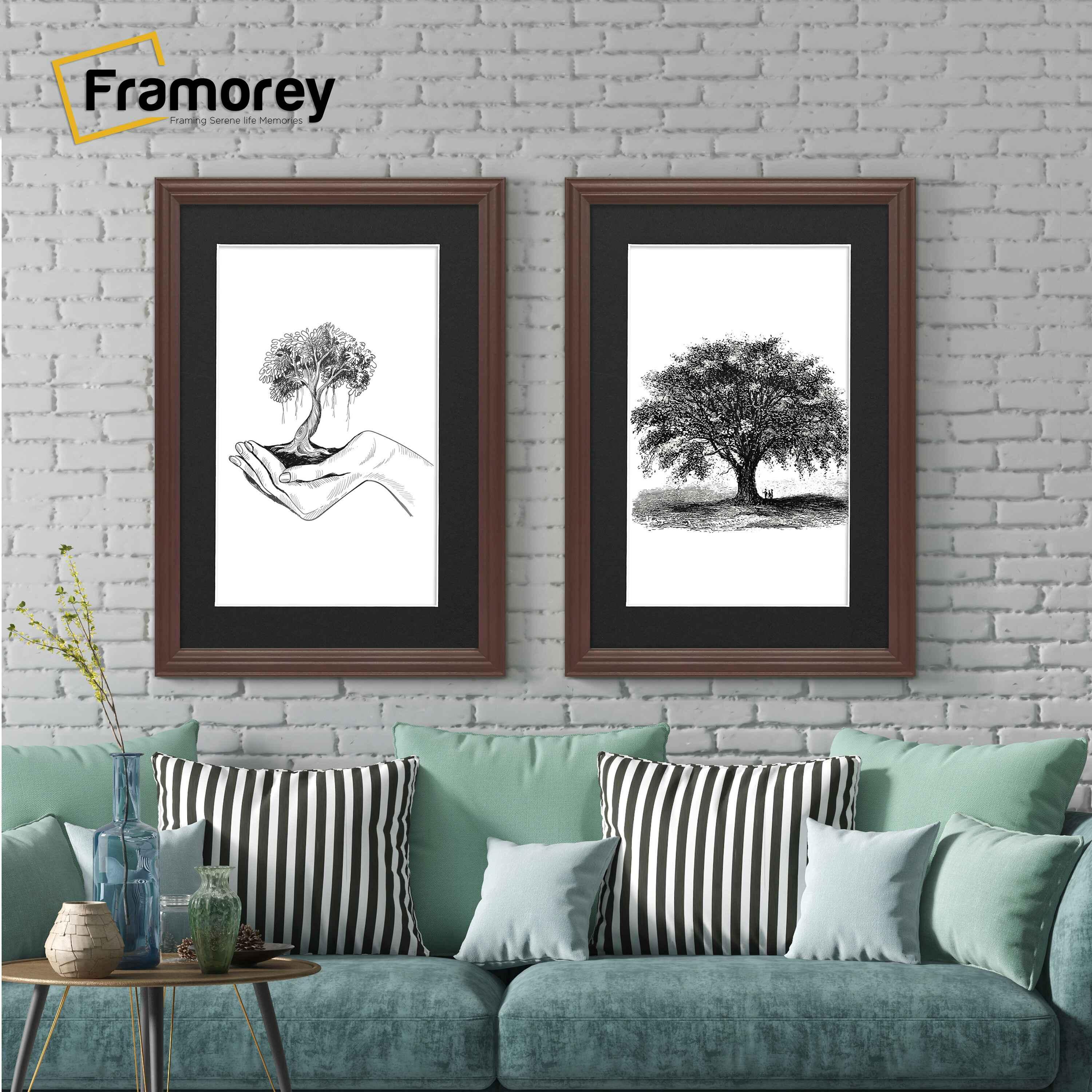Two antique style mahogany picture frames with black mounts displaying black and white artwork hanging above a couch against a brick wall