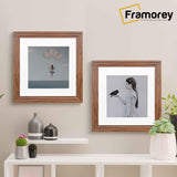 Two Step Style Square Walnut Poster Frame With White Mount hanging on a wall over a table.